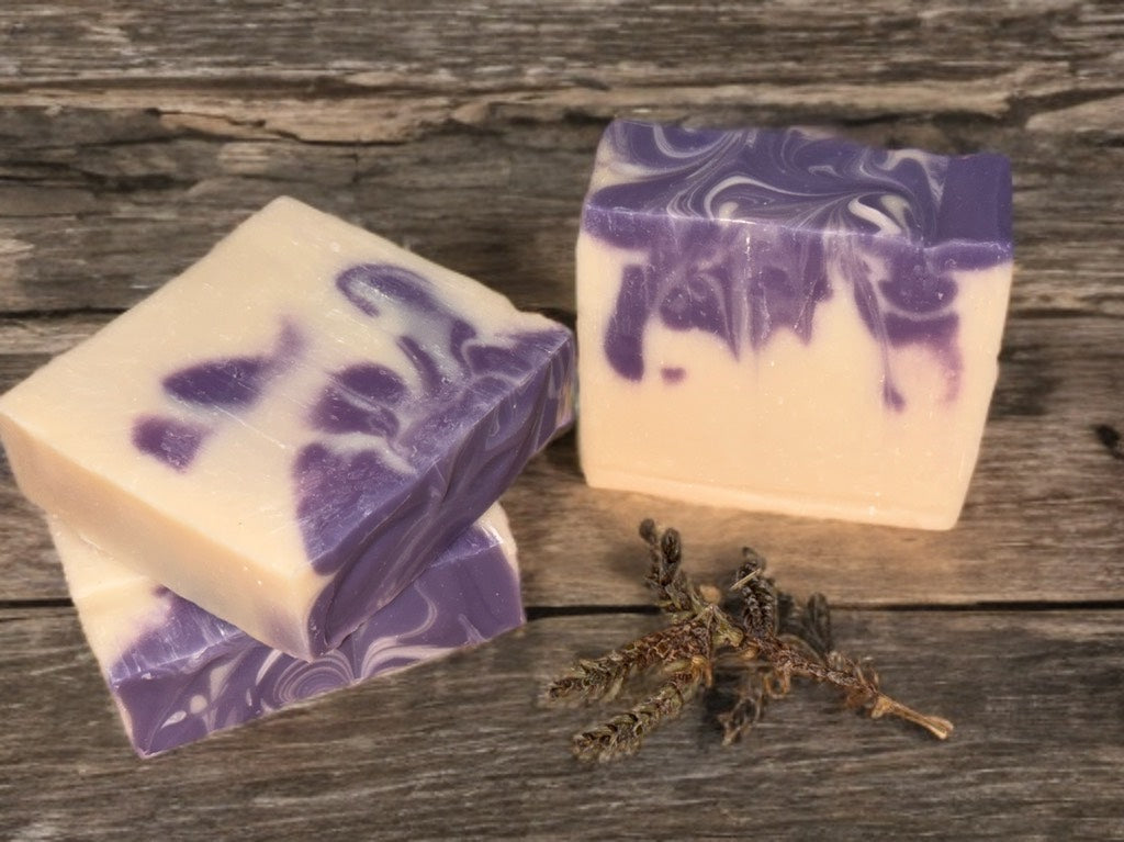 Two bars of swirly purple and white soap with lavender flowers on a wooden surface