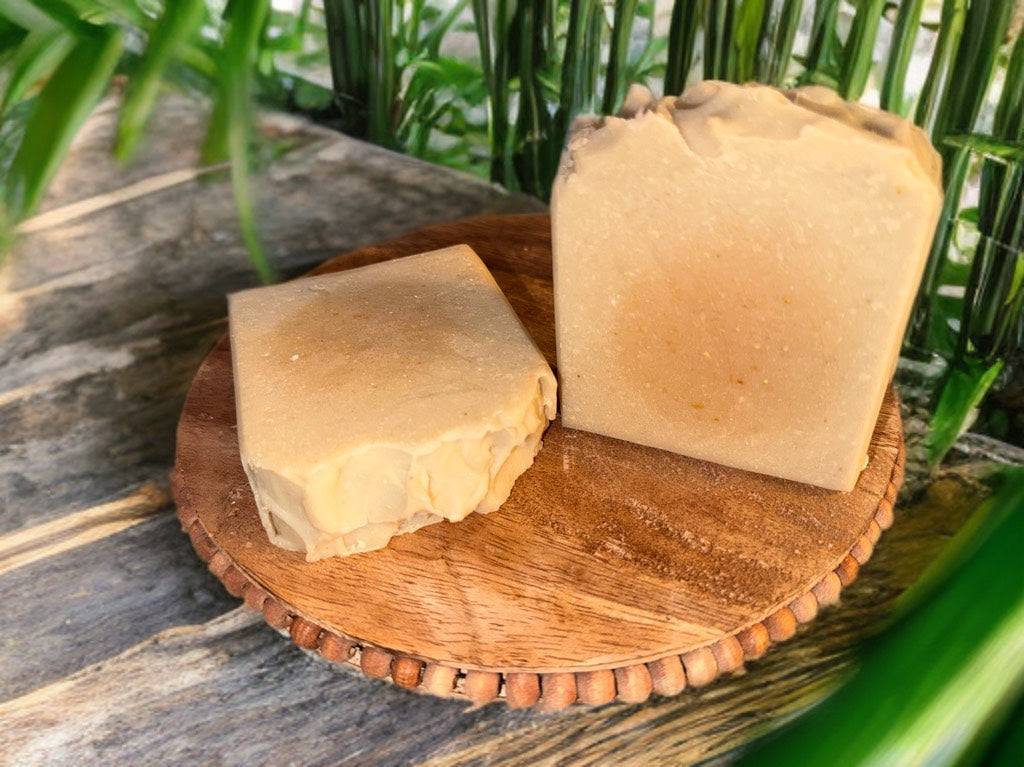 Two pieces of tan soap on a wooden cutting board with a natural background
