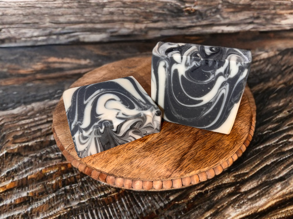 Two bars of black and white marbled soap on a wooden stand with a rustic wooden background.