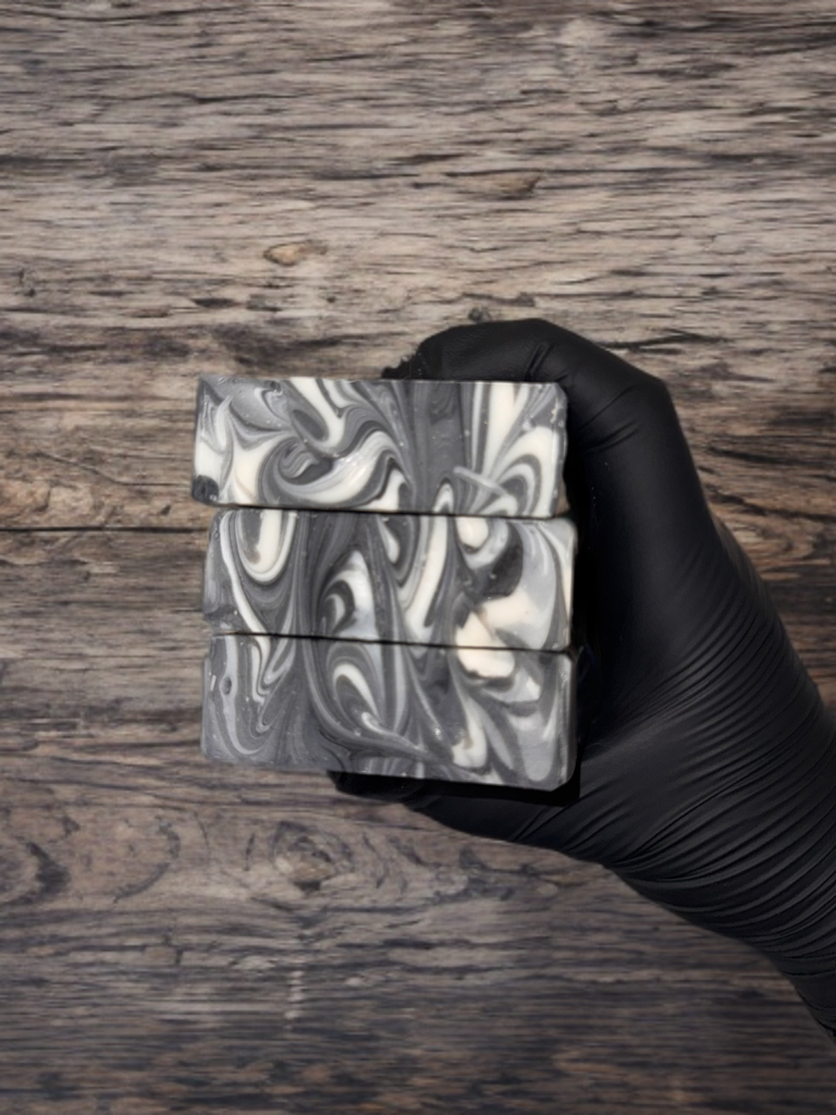 Hand holding three black and white marbled soap bars against a wooden background
