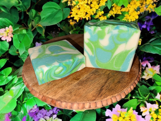 Two green, blue, and white marbled soap bars on a wooden stand with flowers in the background