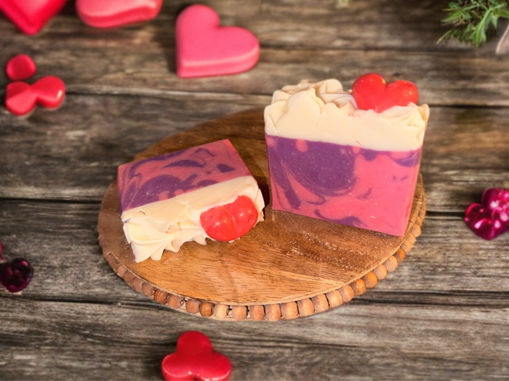 Heart-themed soaps with pink and purple swirls are displayed on a wooden board. Red heart shapes adorn the white swirled top, conveying a warm, romantic tone.