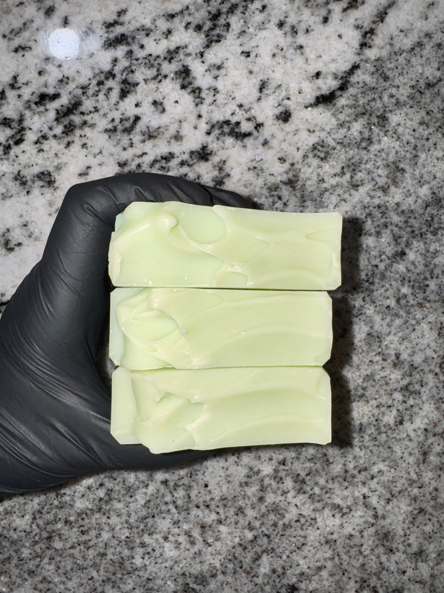 Three bars of soap held by a gloved hand on a gray granite surface