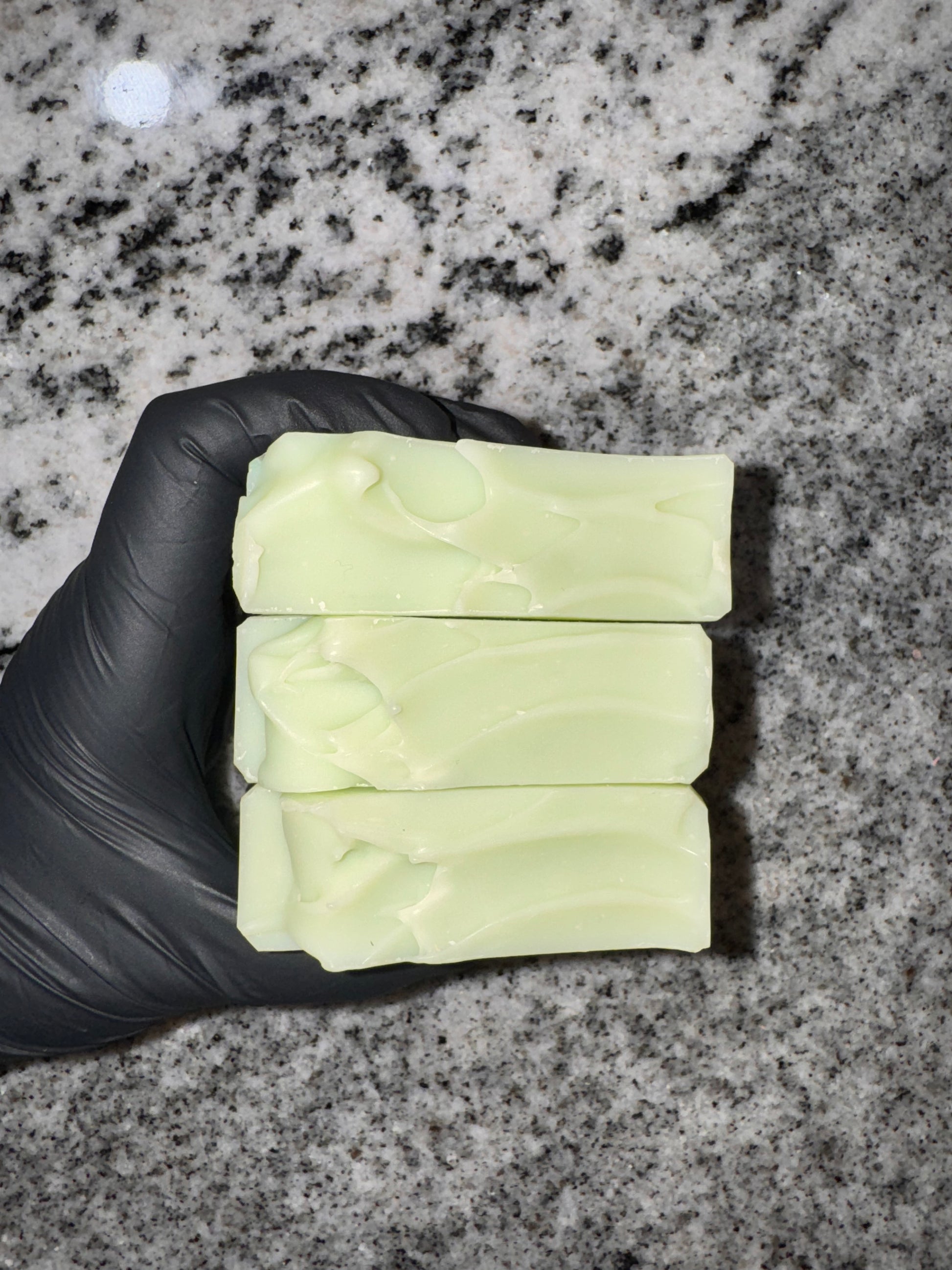 Three bars of soap held by a gloved hand on a gray granite surface